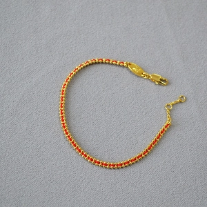 Detail of red braided rope bracelet with gold metal beads and adjustable clasp