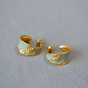 Detail of C-shaped gold earrings with light blue enamel and floral zircon accents