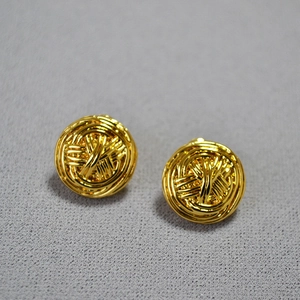 Detailed close-up of golden woven metal ball earrings with intricate twisted line textures