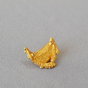 Close-up of golden crescent brooch featuring irregular lava texture and back pin closure