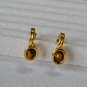 Macro detail of retro gold tiger eye stone earrings on a white knit fabric background