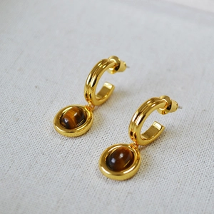 Detail of vintage gold tiger eye hoop earrings on a textured light grey fabric background