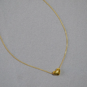 Gros plan détaillé d'un pendentif coeur doré martelé sur une fine chaîne minimaliste