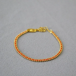 Macro detail of handmade red string bracelet with gold beads and lobster clasp