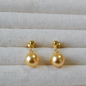Close-up of champagne pearl earrings with gold base in a beige linen display tray
