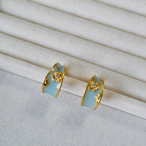 Close-up of gold C-hoop earrings with light blue enamel and zircon daisy detail