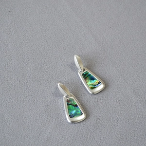Macro detail of geometric silver earrings featuring iridescent rainbow abalone shell inlays