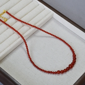 Red agate bead necklace with gradient sizes and gold clasp on jewelry tray