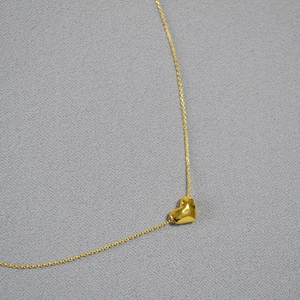 Détail macro d'un pendentif cœur doré poli avec une chaîne fine sur une surface texturée