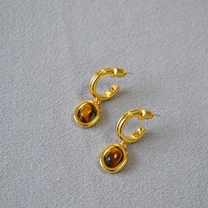 Close-up of golden hoop earrings featuring oval tiger eye stone pendants on grey fabric
