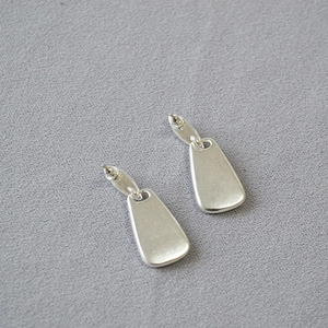 Macro shot of geometric silver earrings with colorful abalone shell inlay on textured fabric