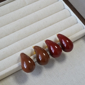 Close-up of enamel water drop earrings in dark red and brown glaze with gold pins