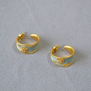Detailed close-up of C-shaped gold earrings with light blue enamel and daisy floral accents