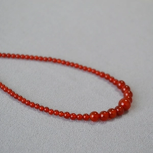 Elegant red agate beaded necklace with gradient sized stones on grey fabric background