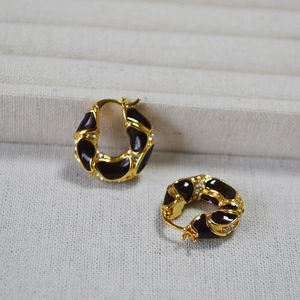 Macro detail of gold-plated hoop earrings with lava texture and burgundy enamel finish
