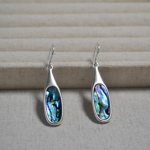 Silver teardrop hook earrings featuring natural colorful abalone shell inlay on beige stand