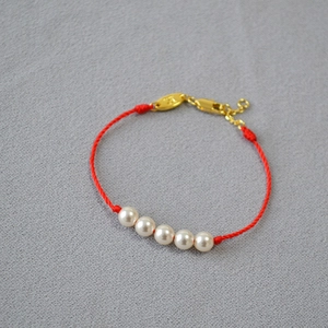 Detailed close-up of handmade red braided cord bracelet with five white pearls and gold clasp