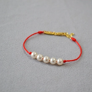 Detailed macro of handmade red cord bracelet with five white pearls and gold clasp