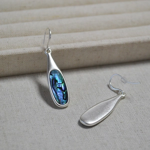 Silver teardrop earrings featuring iridescent abalone shell inlays on linen background
