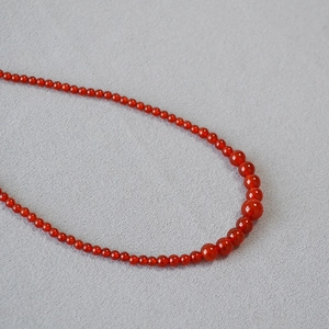 Detailed view of red agate necklace with gradient sized round beads on grey fabric