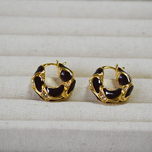 Macro detail of gold-plated hoop earrings with black enamel and sparkling crystals