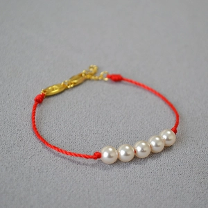 Close-up of five white pearls on a red woven cord bracelet with gold lobster clasp