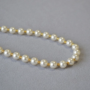 Elegant pearl necklace with golden spacer beads on grey textured background