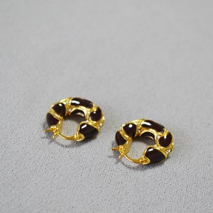 Macro detail of French retro brass gold earrings with burgundy enamel and small crystals