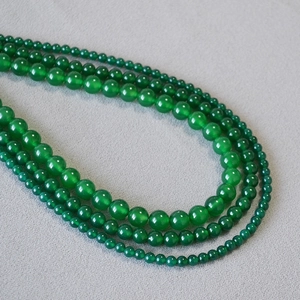Detail shot of multi-sized green agate beads necklace on grey textured fabric