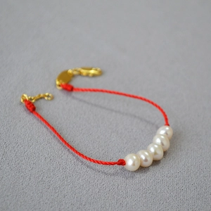 Detail of red woven string bracelet featuring five pearls and golden lobster clasp