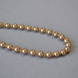 Elegant pearl necklace with champagne gold beads on a textured grey fabric background