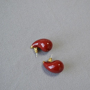 Detailed view of glossy burgundy teardrop earrings with gold-tone backings on fabric
