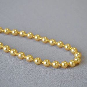 Elegant gold pearl necklace with metallic spacers on a textured grey background