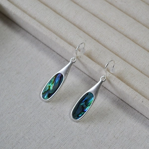 Detail of silver drop earrings featuring iridescent abalone shell inlays on a beige stand