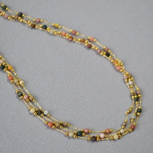 Détail d'un collier multicouche à perles dorées avec pierres fines facettées colorées