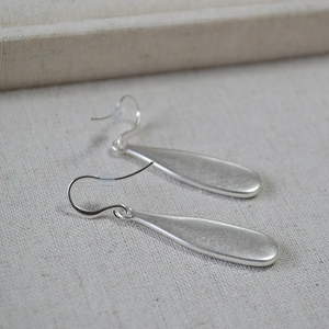 Macro detail of silver teardrop earrings with frosted texture and colorful shell inlay