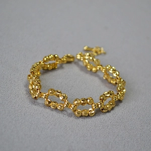 Golden faceted bead woven bracelet with adjustable lobster clasp on grey fabric