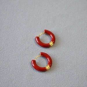 Détail de boucles d'oreilles C en émail rouge et laiton plaqué or sur tissu gris texturé