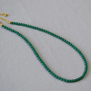 Detail of green agate beaded necklace with gold adjustable chain on grey textured fabric