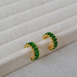 Détail de boucles d'oreilles en C dorées avec pierres de zircone vert émeraude