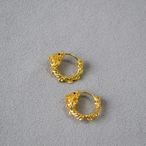 Détail des boucles d'oreilles dragon plaquées or avec écailles 3D sur un tissu gris fin