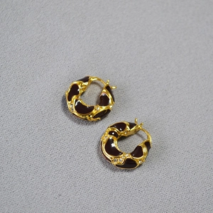 Detail of vintage gold plated brass earrings with burgundy enamel and lava texture