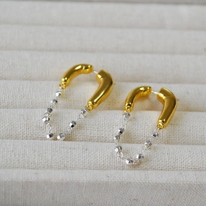 Detail of U-shaped chain drop earrings in gold and silver finish on a fabric jewelry box