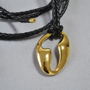 Macro shot of abstract gold-plated brass pendant with black braided cord detailing