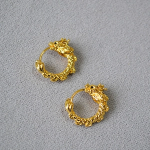 Détail macro de boucles d'oreilles dragon en laiton doré avec textures d'écailles fines