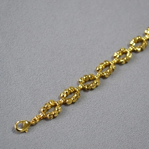 Detailed macro shot of gold-plated beaded chain bracelet with classic lobster clasp closure