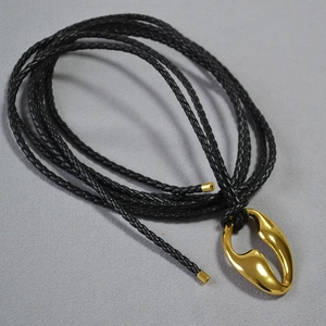 Detail of an abstract gold hollow pendant with black braided leather cord and metal clasps