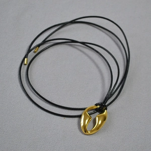 Detail view of a polished gold-plated abstract pendant with a sleek black cord necklace