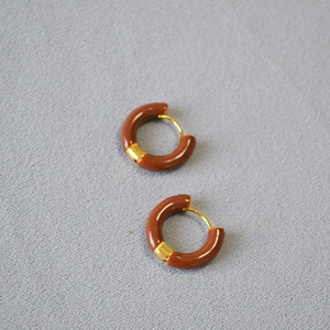 Détail de boucles d'oreilles en émail rouge avec fermoir en laiton doré sur fond tissu
