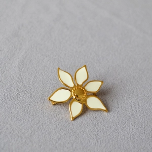 Detailed close-up of a white enamel flower brooch with elegant gold plating finish